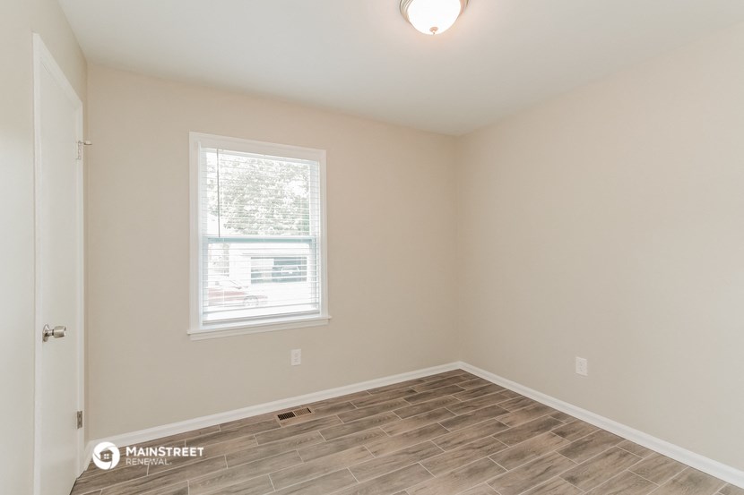 the spacious living room with wood flooring and a window