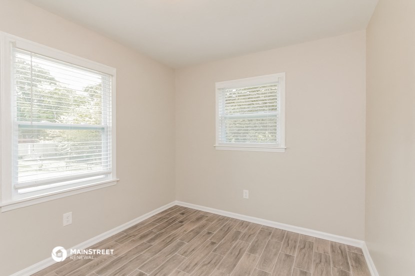 the living room of a home with wood floors and two windows