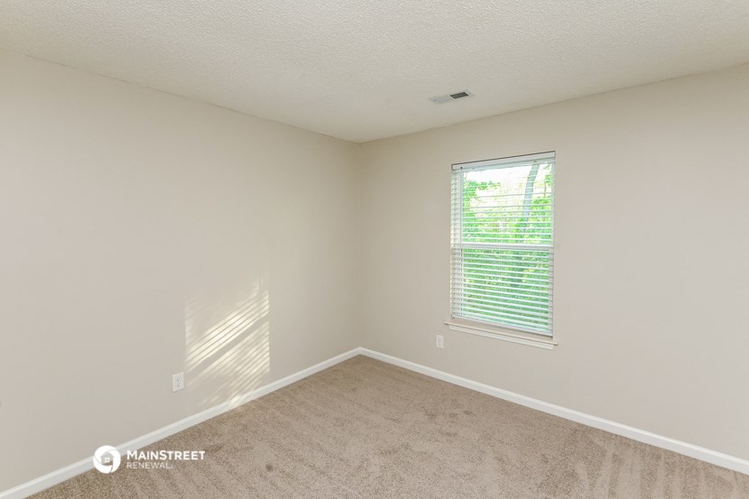 a spacious bedroom with carpet and a window