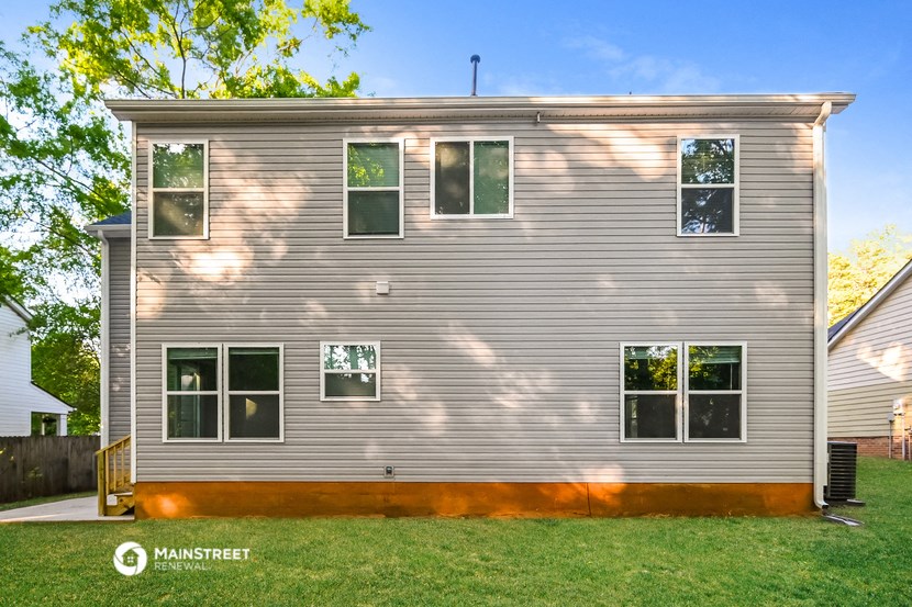 the back of a gray house with green grass and trees