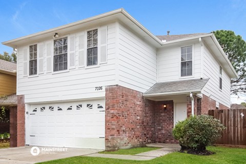 a white house with a brick wall and a white garage door