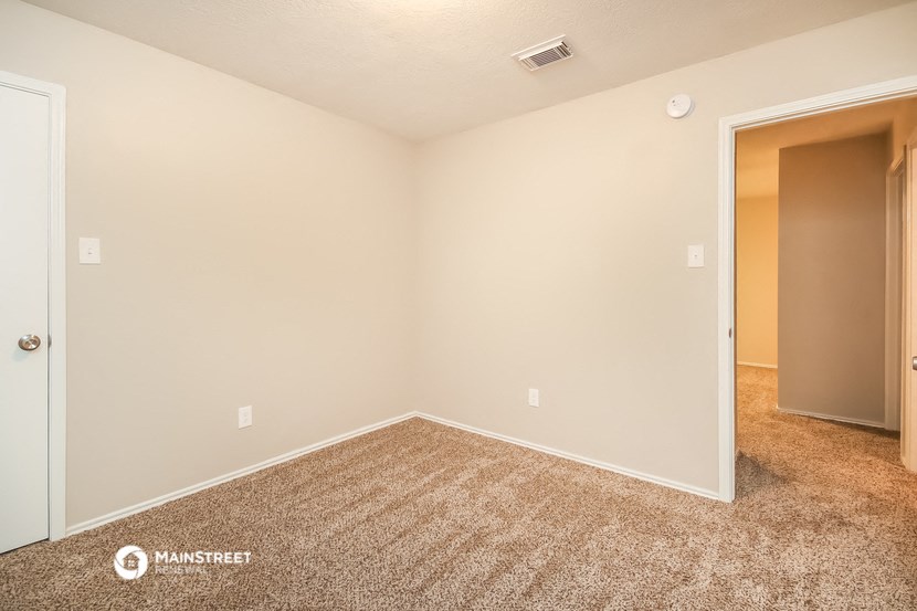 the living room of an apartment with carpet and a door to a closet