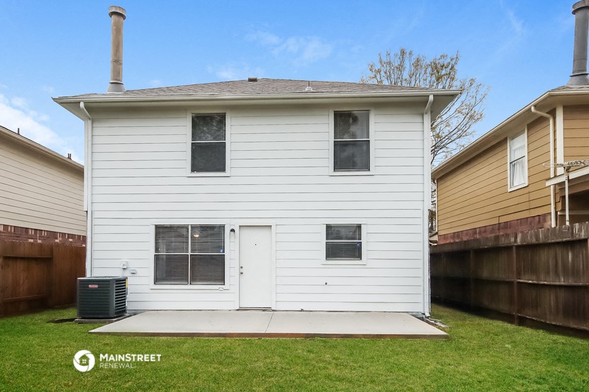 the back of a white house with a yard and a wooden fence