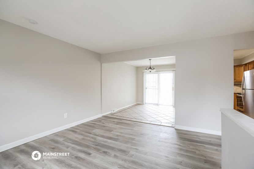 the living room and dining room of an apartment with white walls and wood flooring