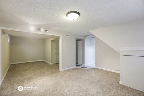 a spacious living room with carpet and a door to a hallway