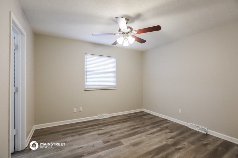 the spacious living room with wood flooring and a ceiling fan