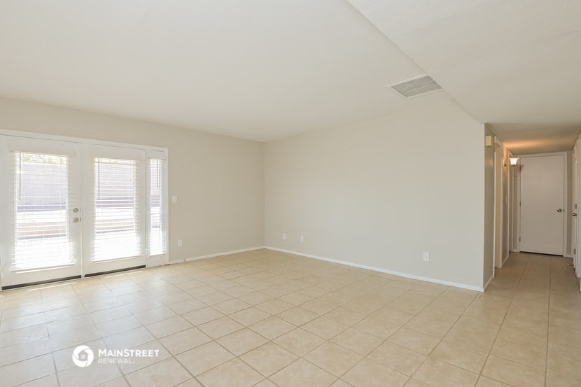 an empty living room with a door to a hallway and a tiled floor