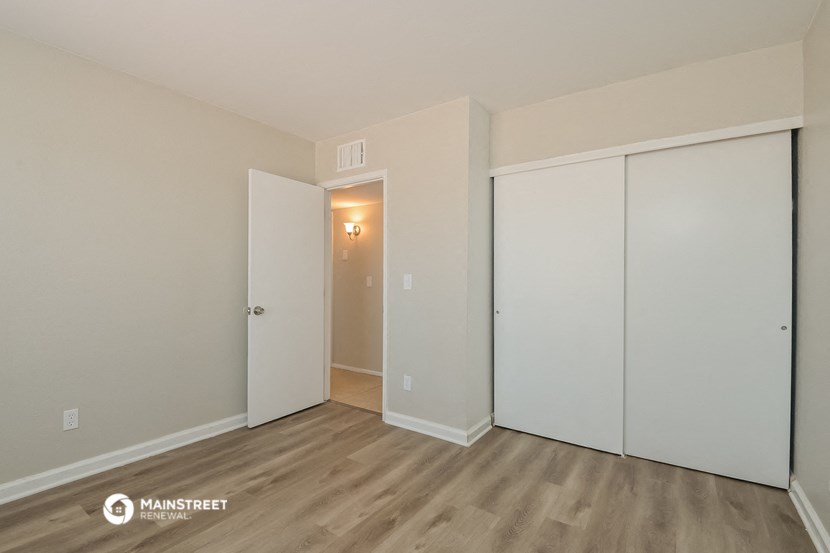 the living room of an apartment with white walls and wood flooring