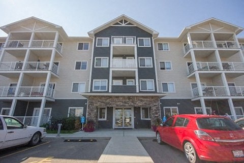 A red car is parked in front of a building with a stone entrance.