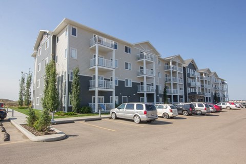 A row of apartment buildings with cars parked in front.