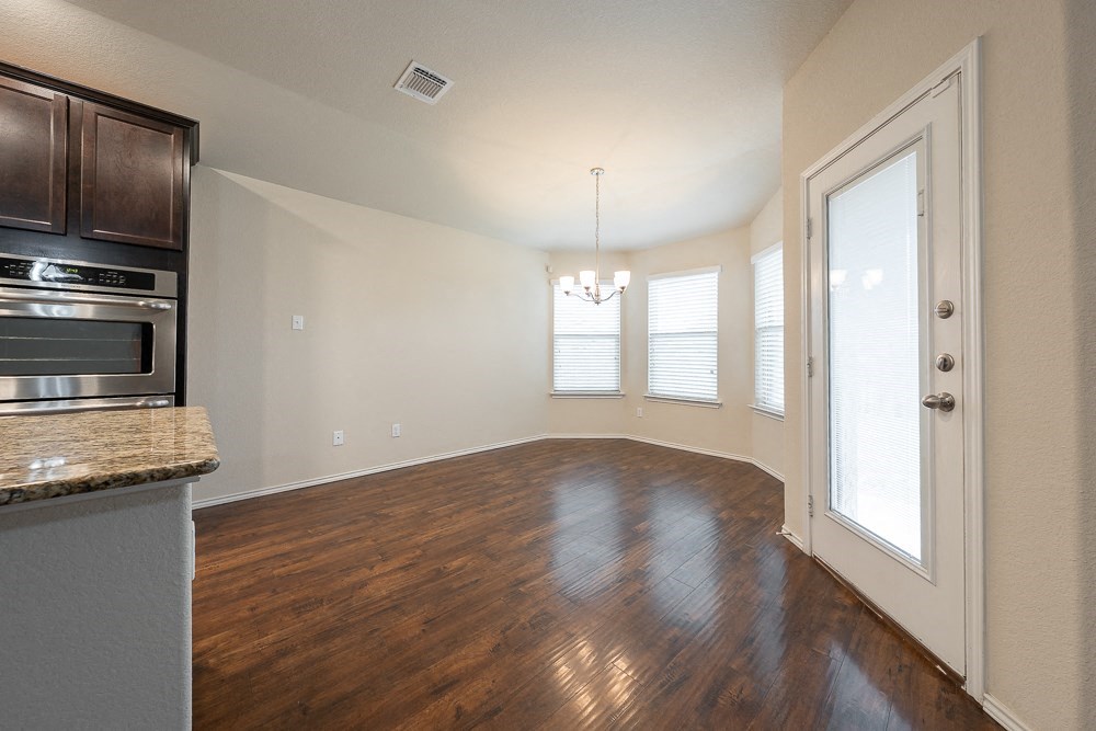 an empty living room with hardwood flooring and a door to a kitchen