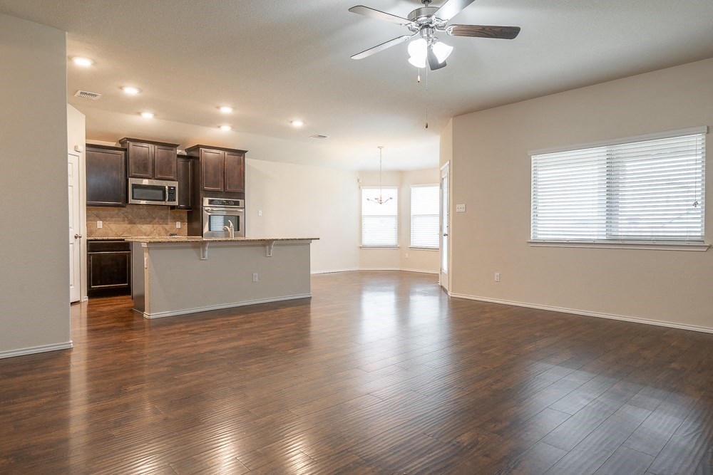 an empty living room with a kitchen and a ceiling fan