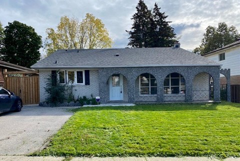 A house with a grey roof and a white door is surrounded by a green lawn.