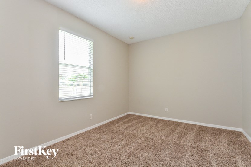 A room with a carpeted floor and a window with blinds.