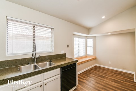 A kitchen with a sink, dishwasher, and a window with blinds.