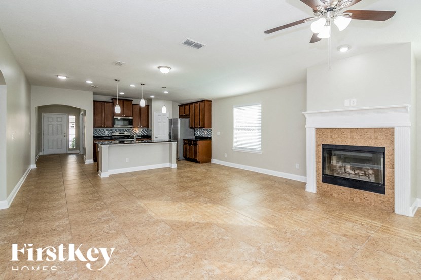 A spacious living room with a fireplace and a kitchen in the background.