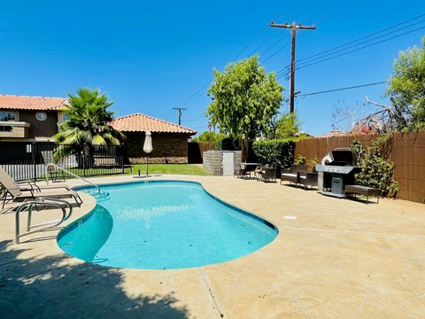 A pool in a backyard with a patio and a fence.