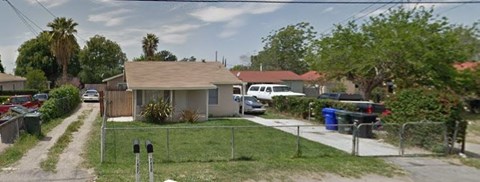 A house with a brown roof is surrounded by a green lawn and a fence.