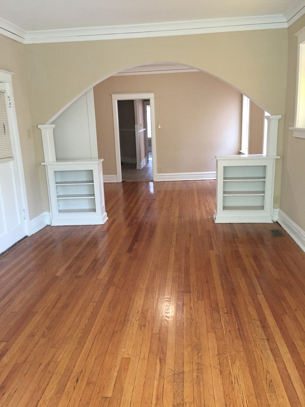 an empty living room with a hard wood floor and a hallway with two dressers