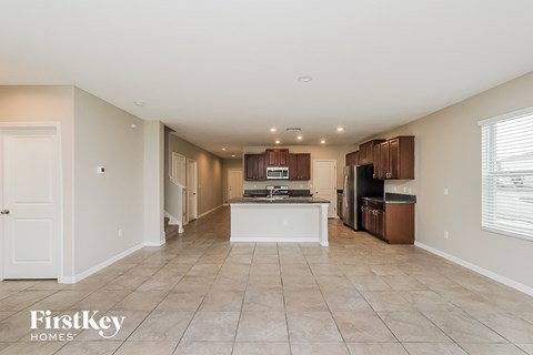 A spacious kitchen and living room with white walls and tile flooring.