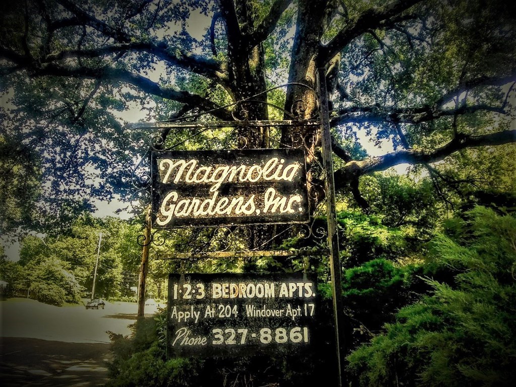 A sign for Magnolia Gardens, Inc. is displayed in front of a tree.