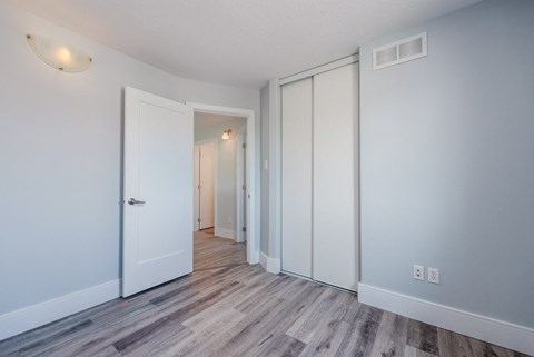 a bedroom with white walls and wood flooring and a closet
