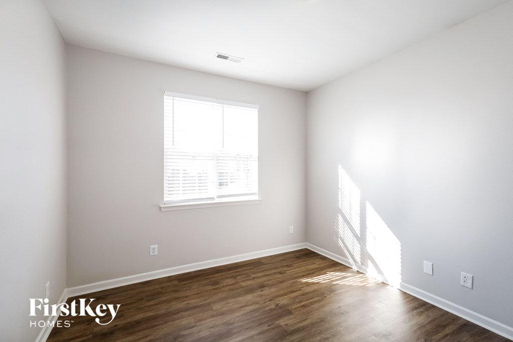 a bedroom with white walls and wood floors and a window