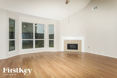 A large empty room with a fireplace and wooden floors.
