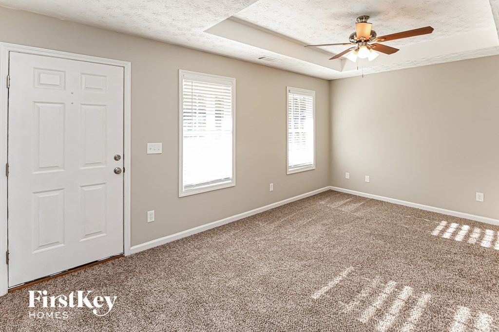 A room with a carpeted floor, a ceiling fan, and a door.