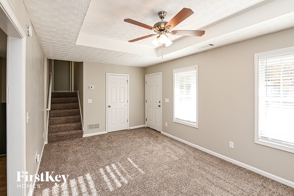 A room with a carpet, a ceiling fan and a staircase.