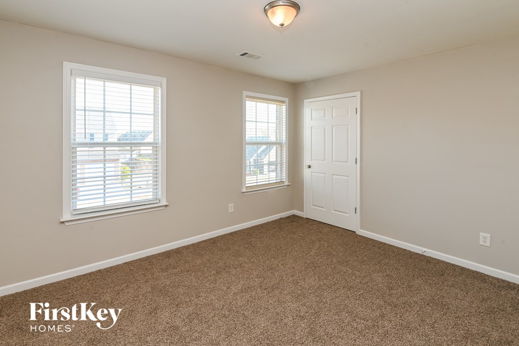 a bedroom with a carpeted floor and a door and two windows