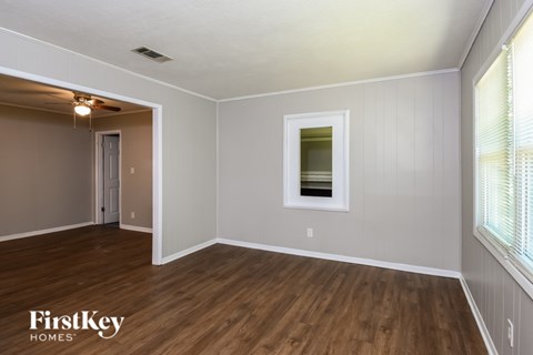 A room with wooden floors and white walls, with a window on the right side.