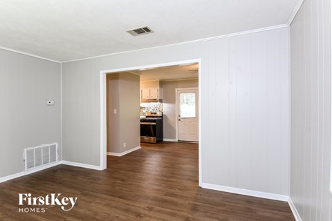 A room with wooden floors and white walls, with a doorway leading to another room.