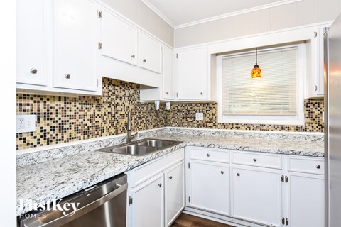 A kitchen with white cabinets and a marble countertop.