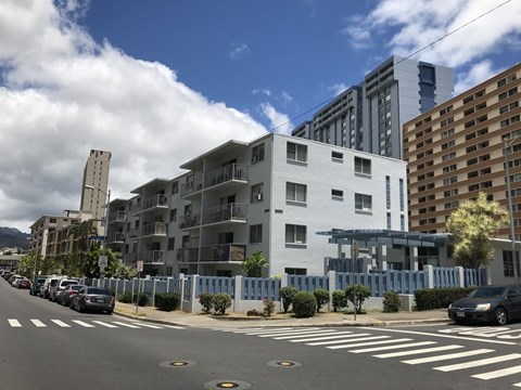 A street view of a residential area with cars parked on the side of the road and modern buildings in the background.