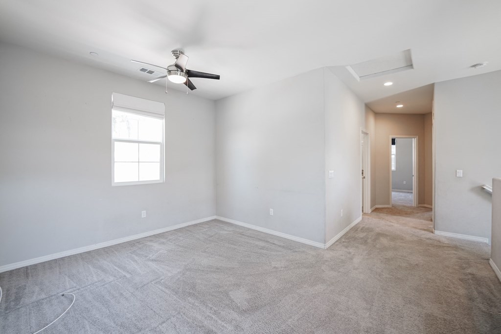 an empty living room with a ceiling fan and white walls