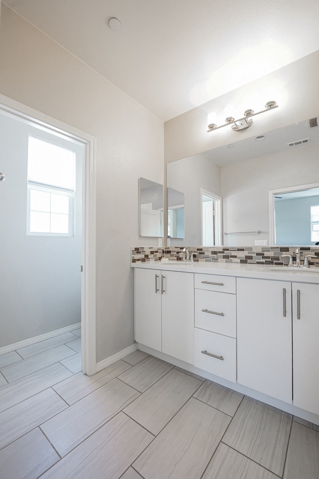 an empty bathroom with white cabinets and a large mirror