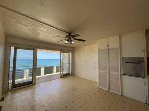 A spacious room with a ceiling fan and a view of the ocean through the sliding glass doors.