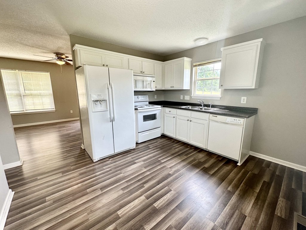 A kitchen with white appliances and wooden floors.