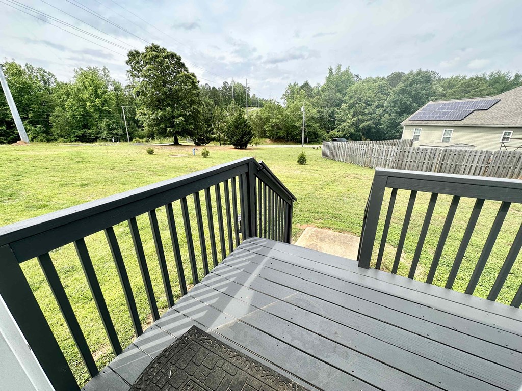 A wooden deck with a black railing overlooks a green lawn.