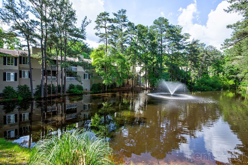 Apartments for Rent in Marietta GA - Arlington Park - Large Pond with Fountain and Surrounding Greenery, Trees, and Building Exterior Views
