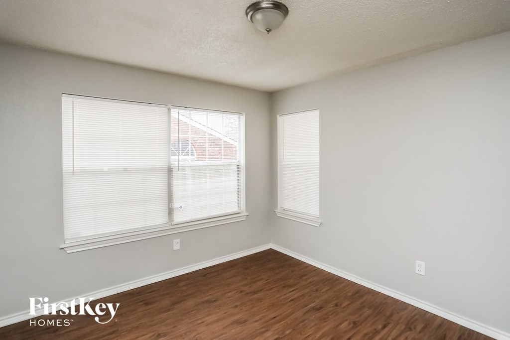 the living room of an apartment with wood flooring and two windows
