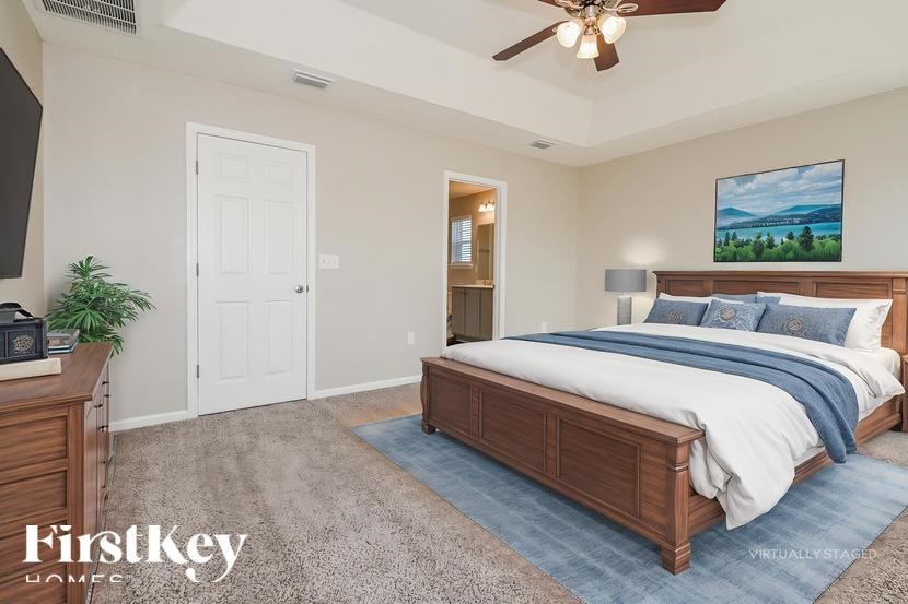 A bedroom with a large bed, a ceiling fan, and a painting on the wall.