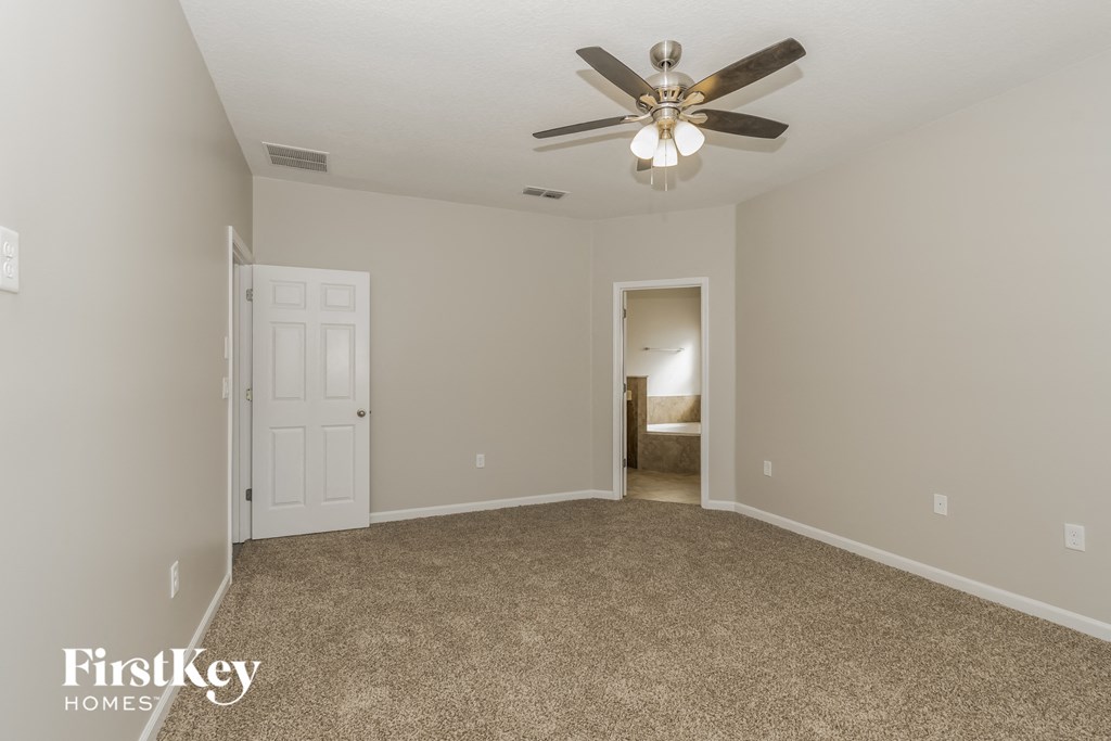 an empty living room with a ceiling fan and a door to a bedroom