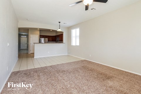 an empty living room with a kitchen and a ceiling fan