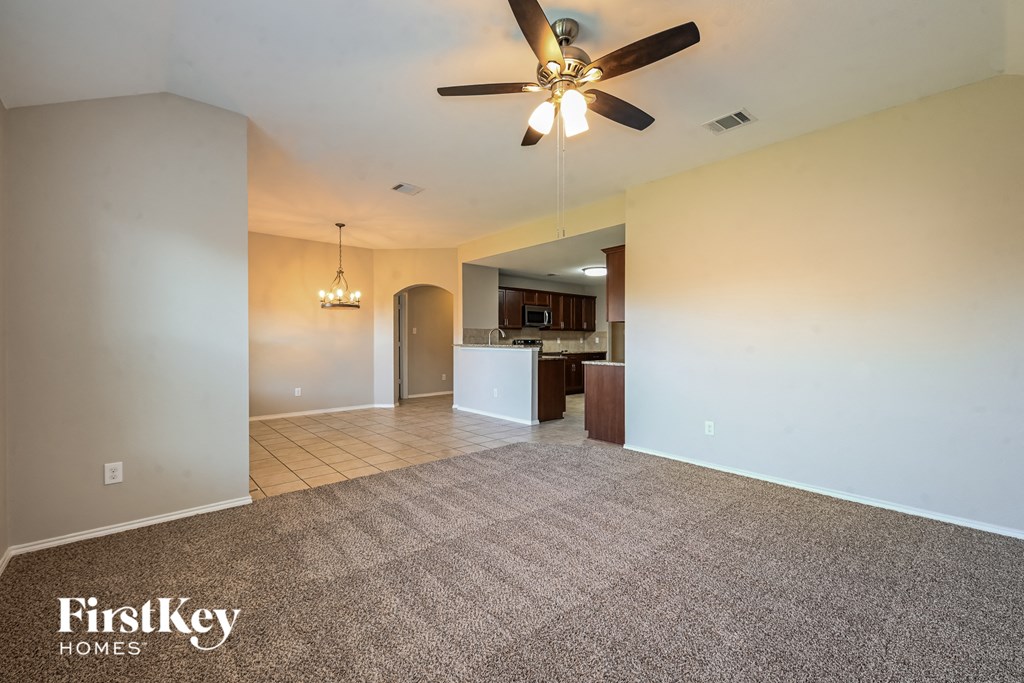 an empty living room with a ceiling fan and a kitchen
