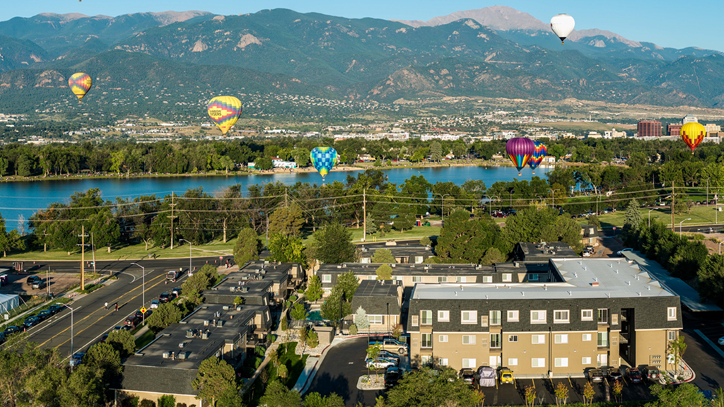 balloons flying over the city and lake with mountains in the background