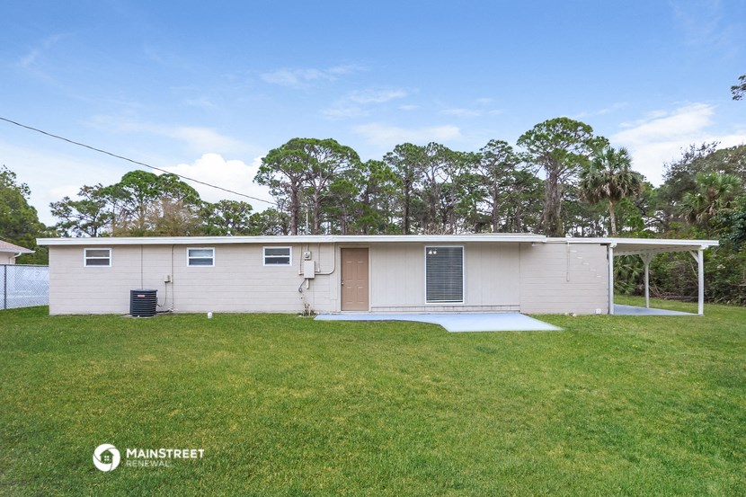 a small white house with a grassy yard and trees in the background