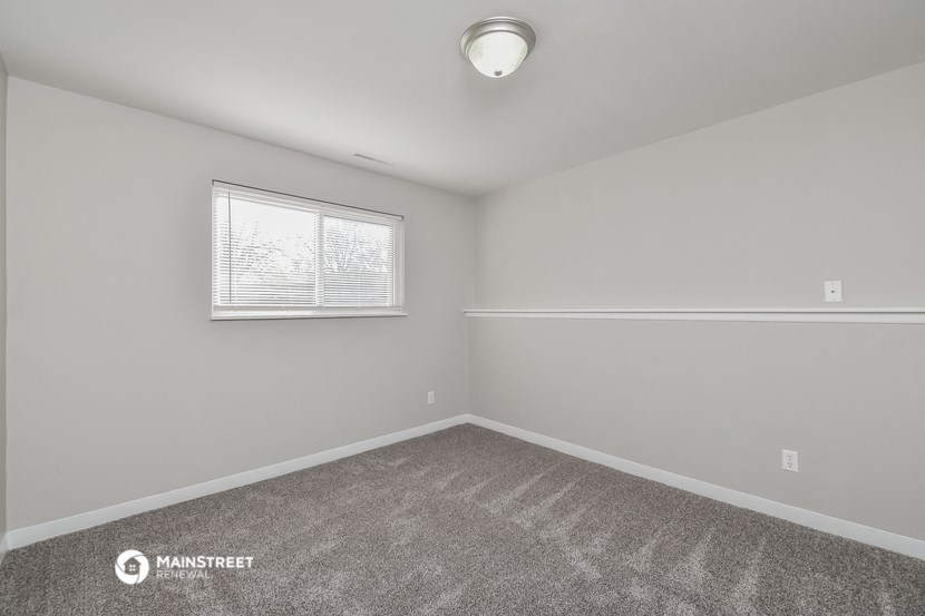 the spacious bedroom has carpeted flooring and a window