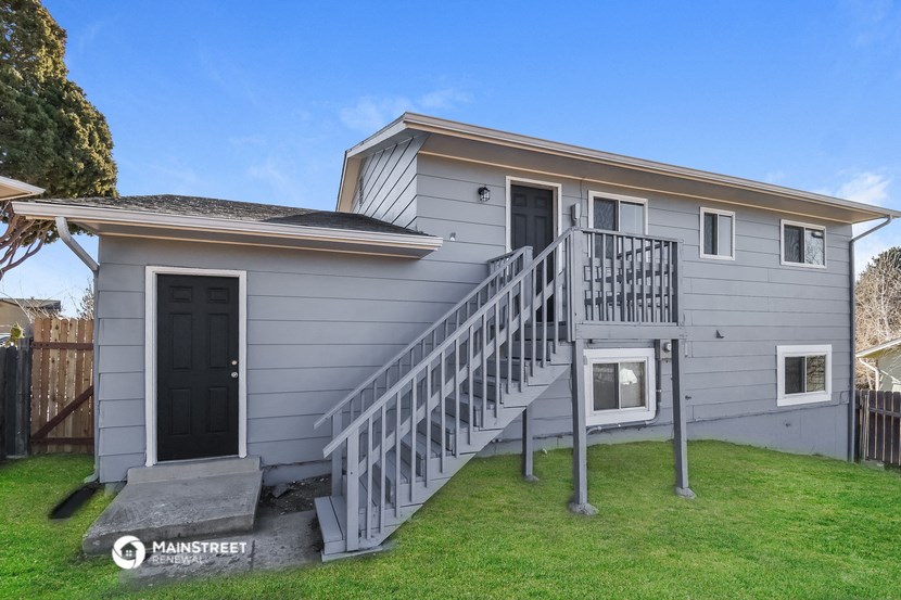 a small gray house with a stairway and a backdoor to a yard